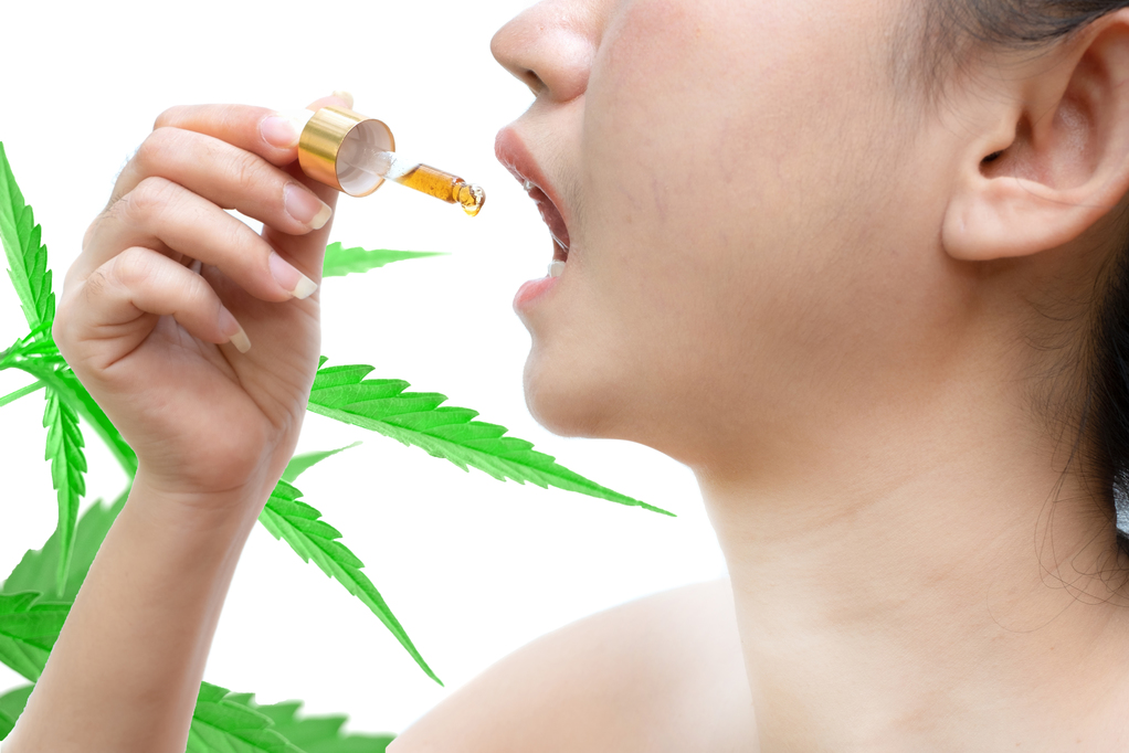Femme tenant un compte-gouttes d'huile de cannabis sublinguale à fond blanc