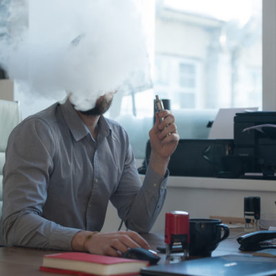 homme travaillant avec un ordinateur au bureau et vapotant une cigarette électronique