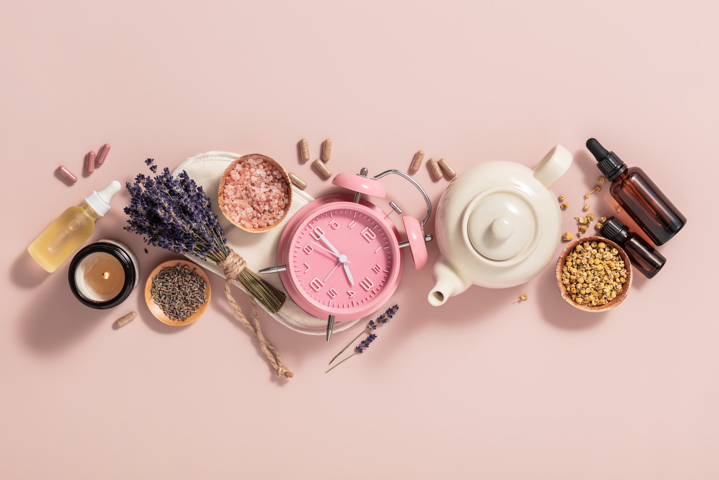Réveil, masque de sommeil, herbes médicinales, capsules, thé à la camomille et huile d'aromathérapie sur fond rose