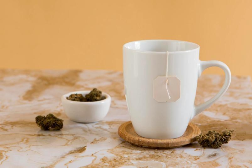 une tasse blanche avec un sachet de thé à l'intérieur et du chanvre sur la table