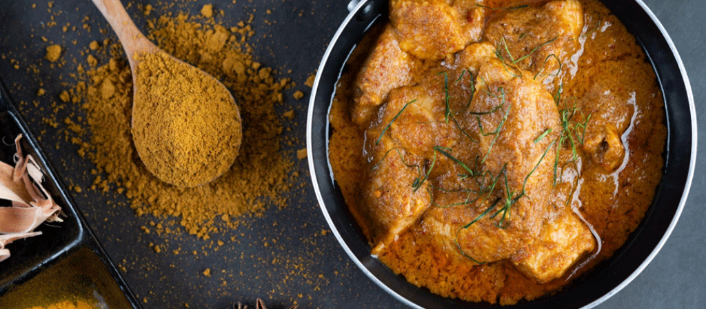 poudre de curry sur une louche, plat de curry de poulet sur un bol